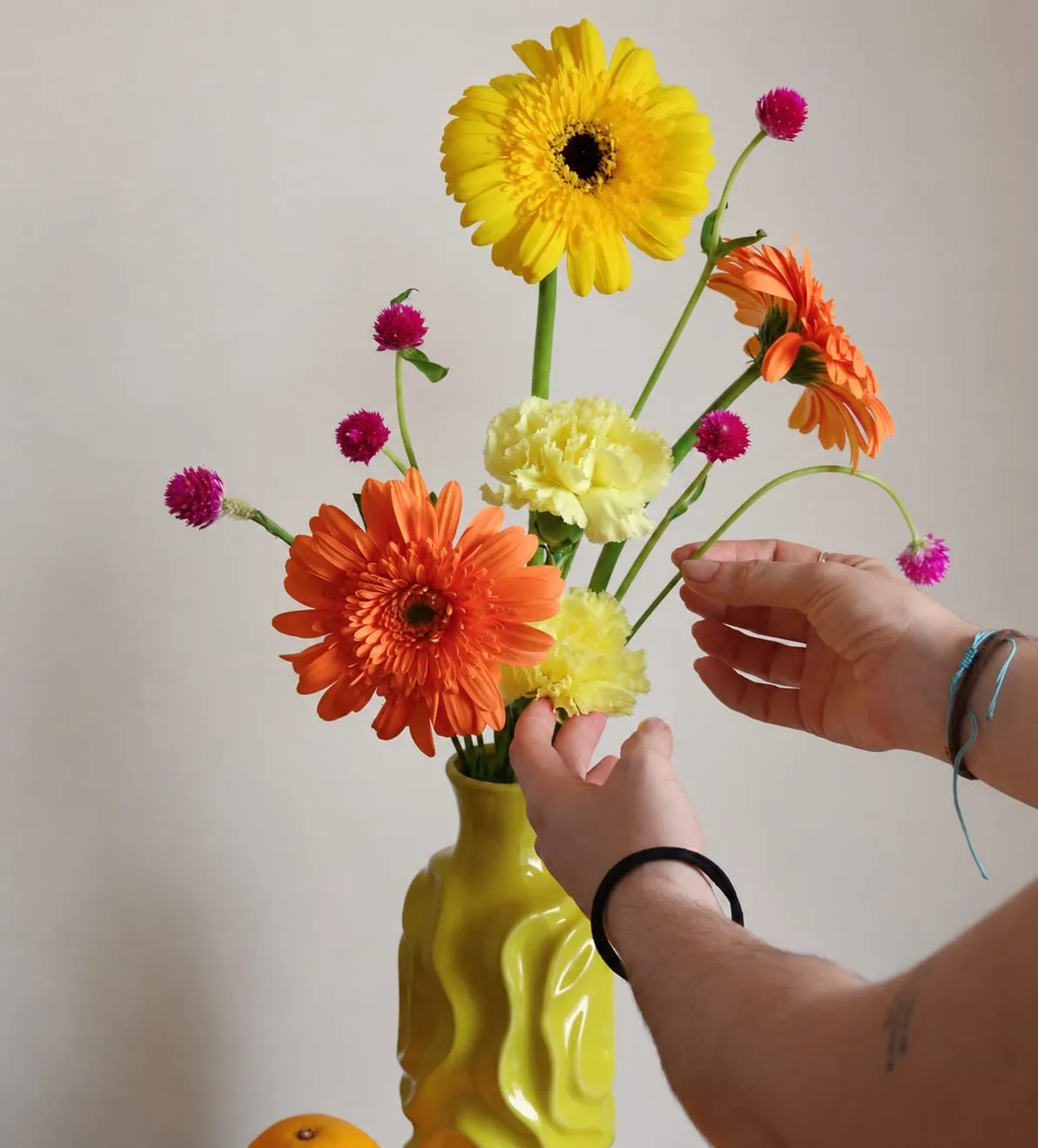 Manos colocando gerberas, claveles y amarantos en un jarrón amarillo