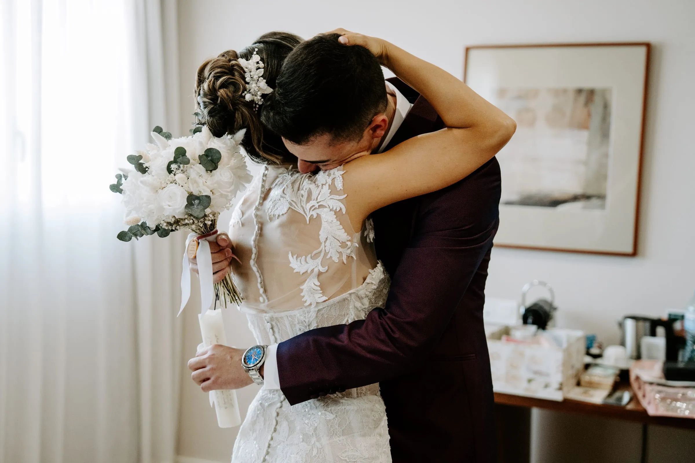 Los novios se abrazan; ella sostiene un ramo de flores blancas