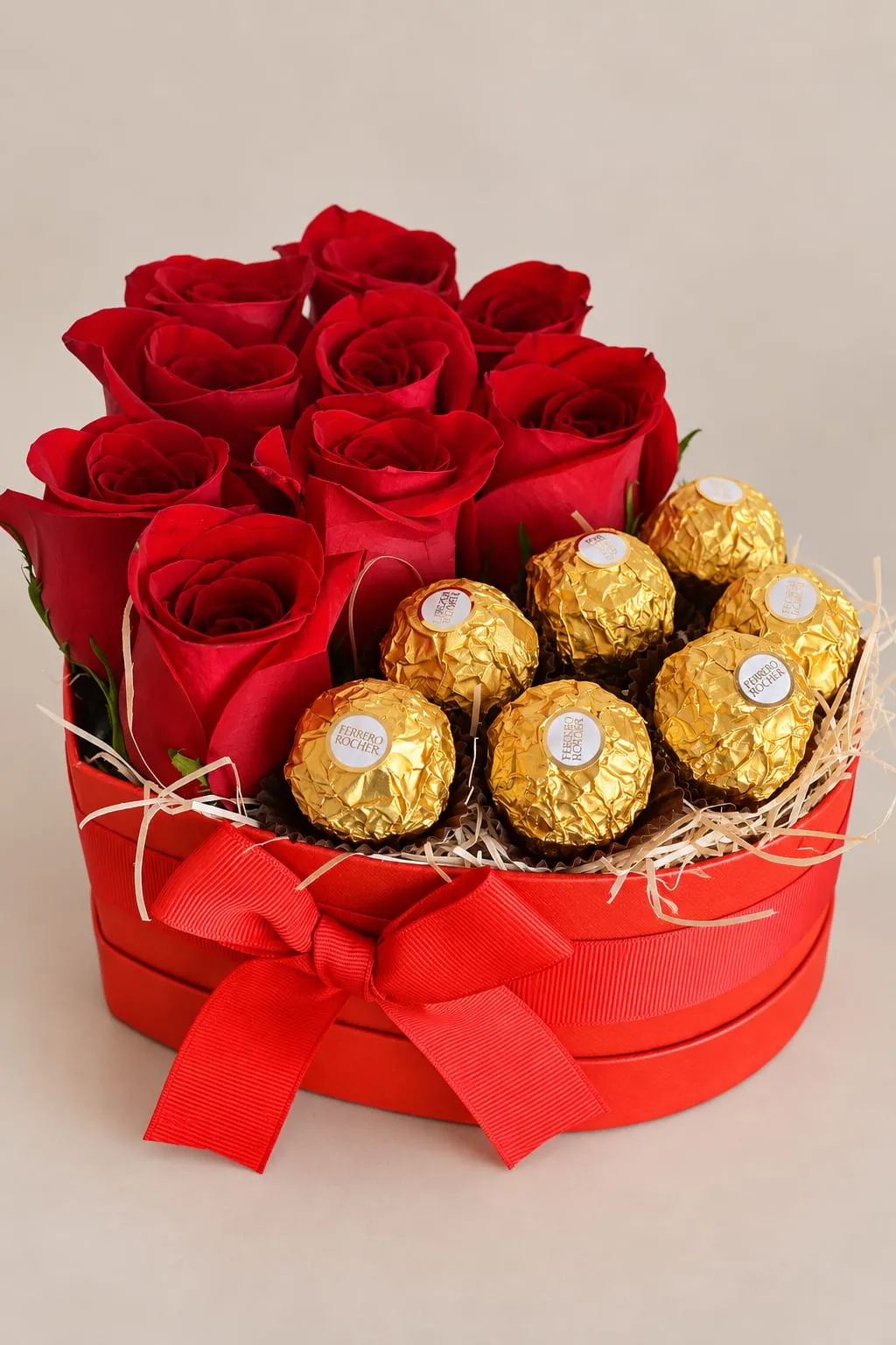 Caja roja con forma de corazón llena de rosas rojas y bombones envueltos en papel dorado, cerrada con un lazo rojo.