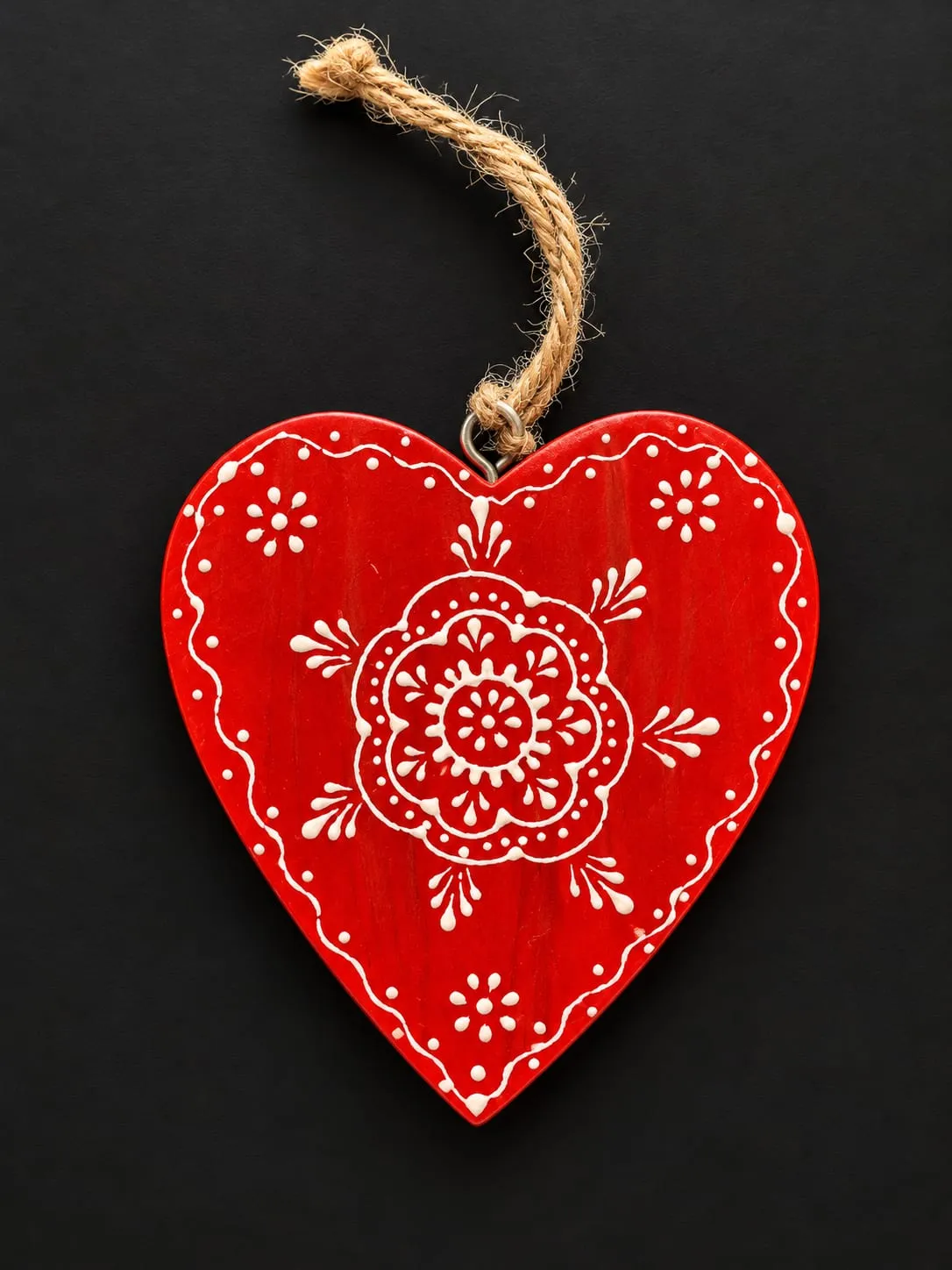 Corazón de madera rojo con un mandala floral pintado en blanco y un cordel de yute.