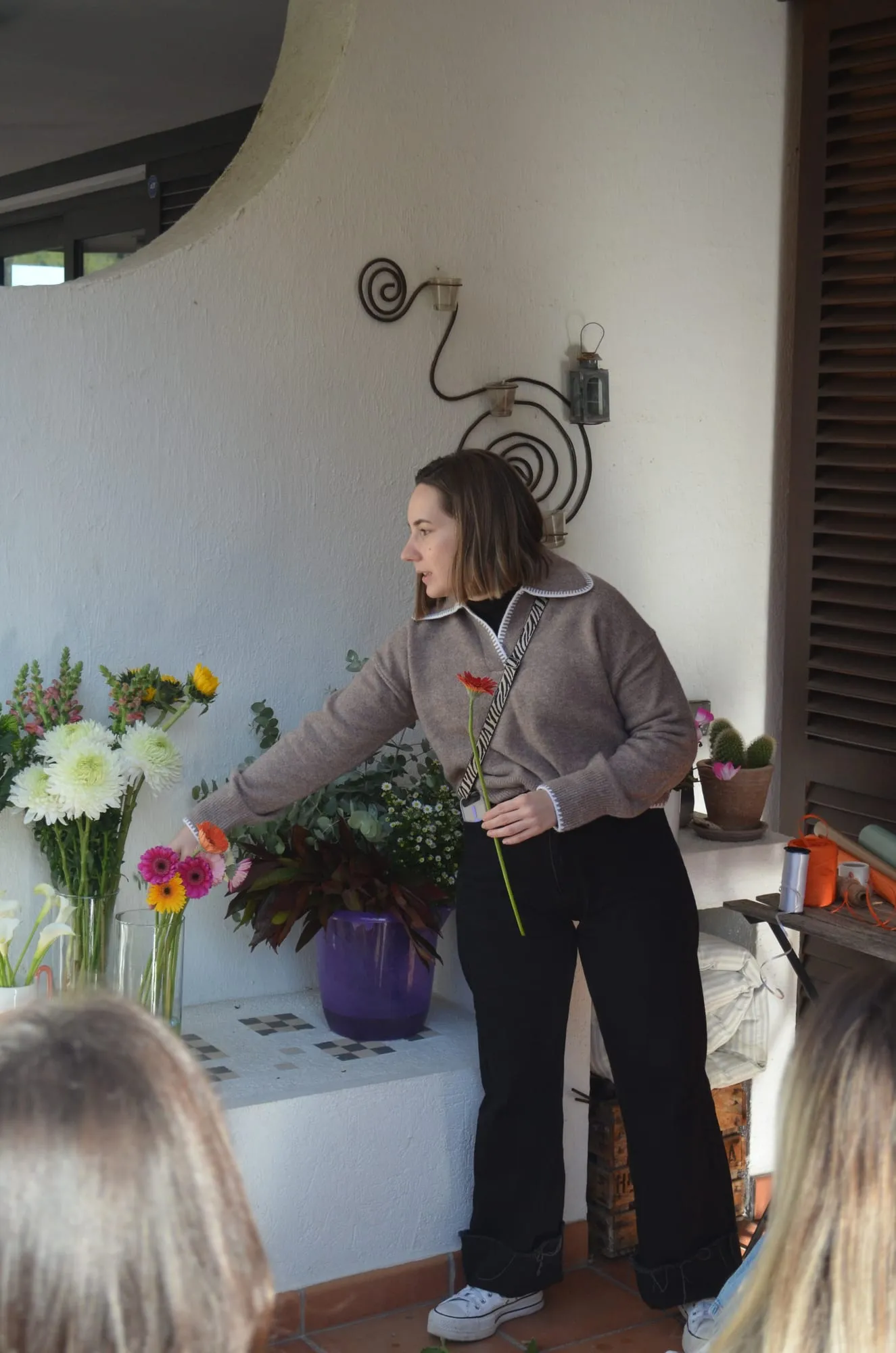 Una chica elige una gerbera entre los jarrones de flores colocados en un banco de obra blanco de la terraza