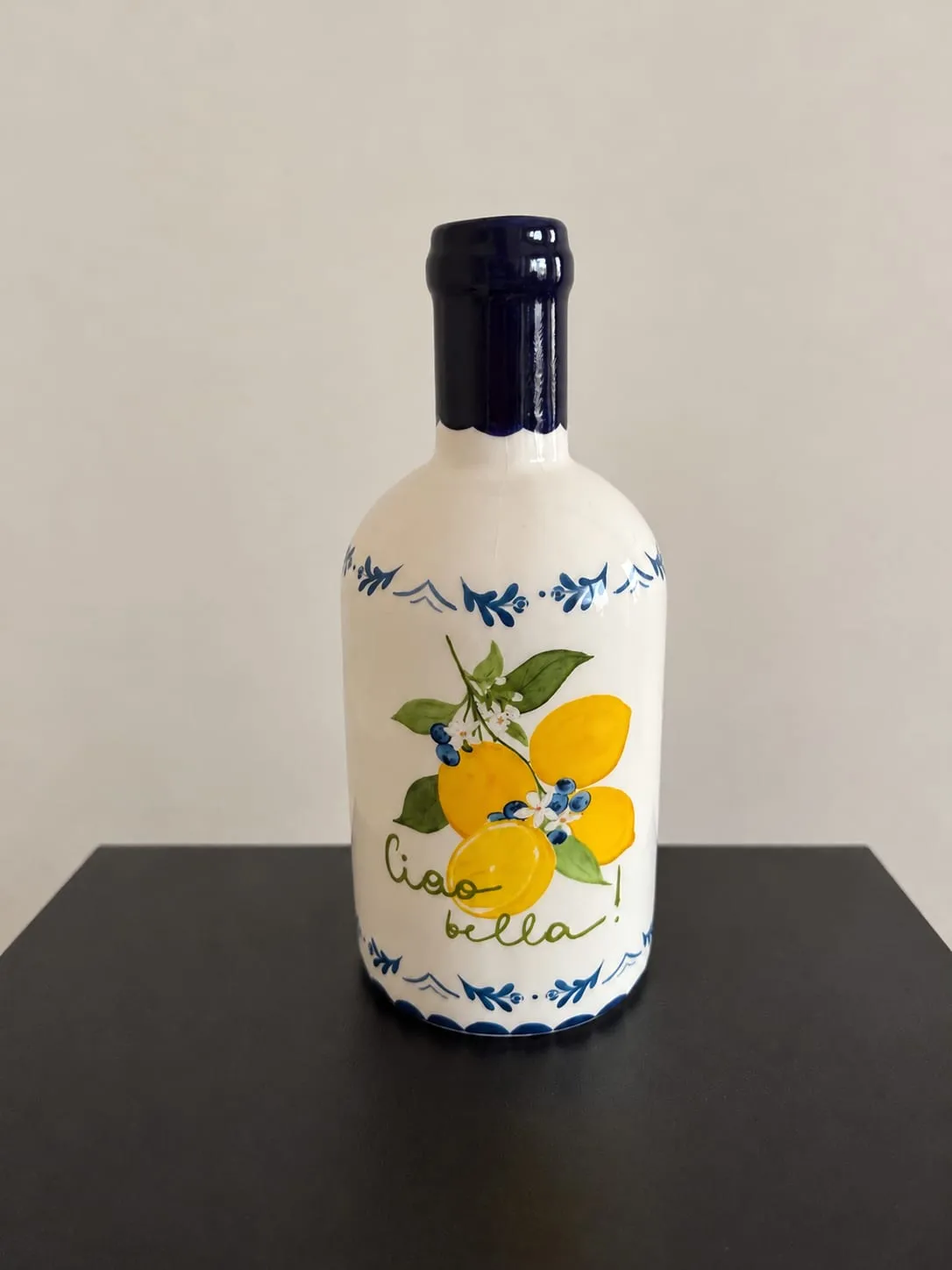 Jarrón de cerámica blanca con forma de botella y cuello azul, con limones pintados y el texto «Ciao bella!».