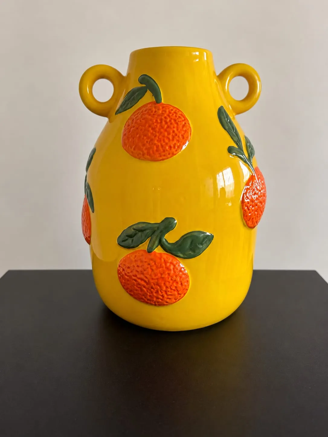 Jarrón de cerámica amarilla con dos asas redondas y naranjas con hojas en relieve.