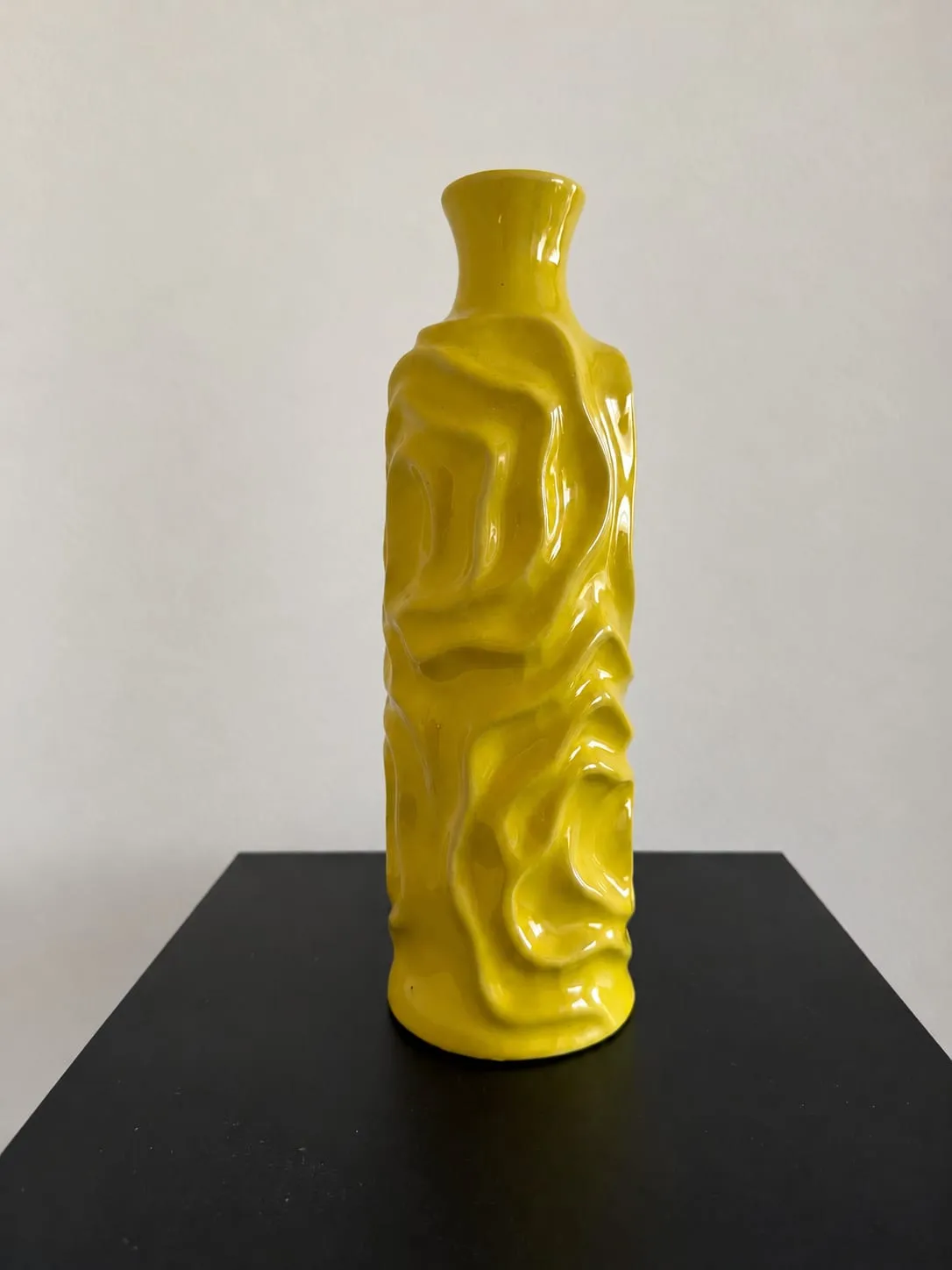 Jarrón alto y estrecho de cerámica amarilla brillante con relieve ondulado.