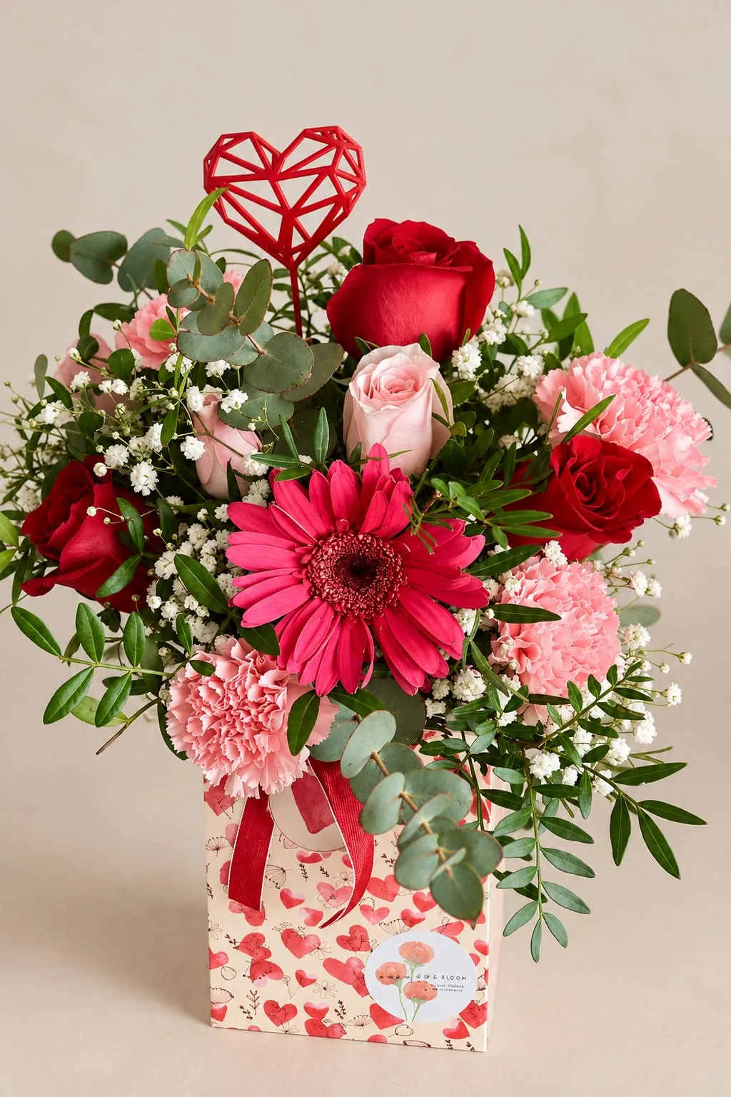 Rosas rojas y rosas, una gerbera fucsia, claveles rosas y paniculata en una caja estampada con corazones, con un corazón rojo de adorno.