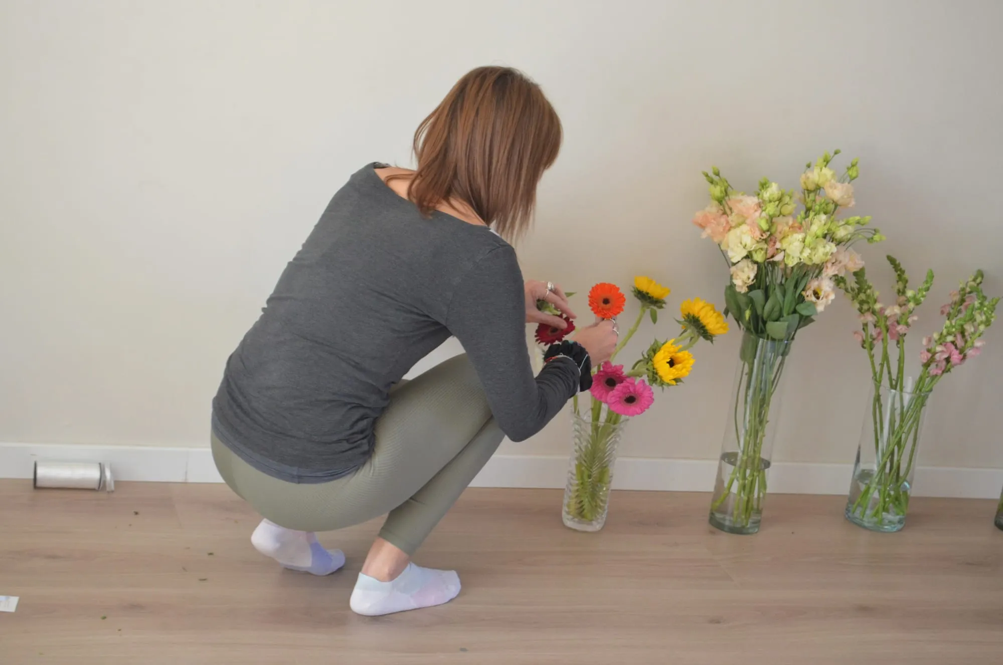 Una participante en cuclillas coge una gerbera de los jarrones con gerberas, girasoles, alstroemerias y bocas de dragón