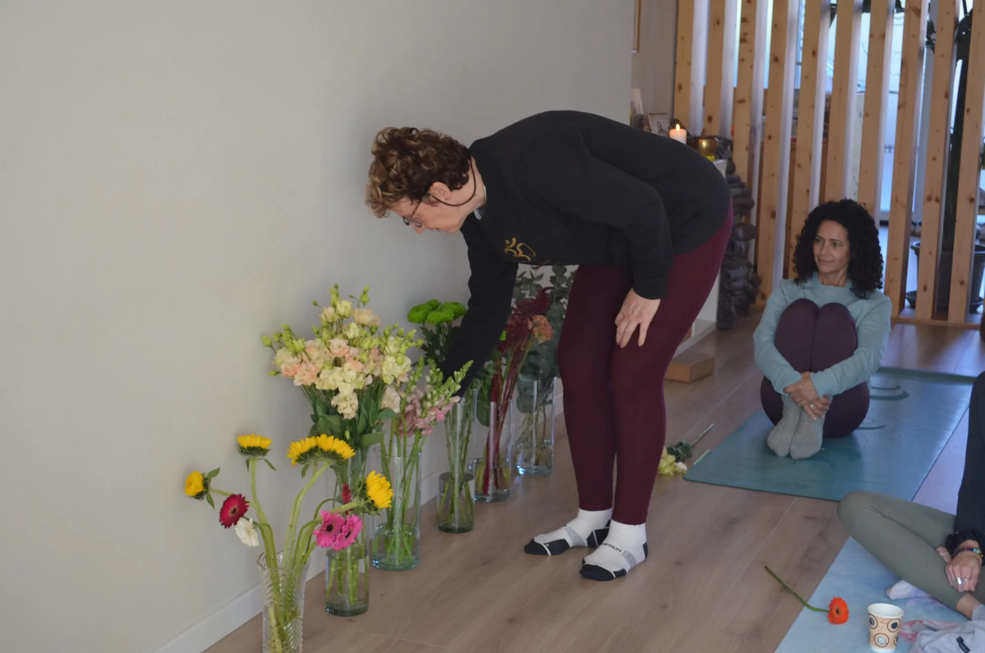 Una participante con gafas se inclina sobre los jarrones para escoger flores mientras otra espera sentada