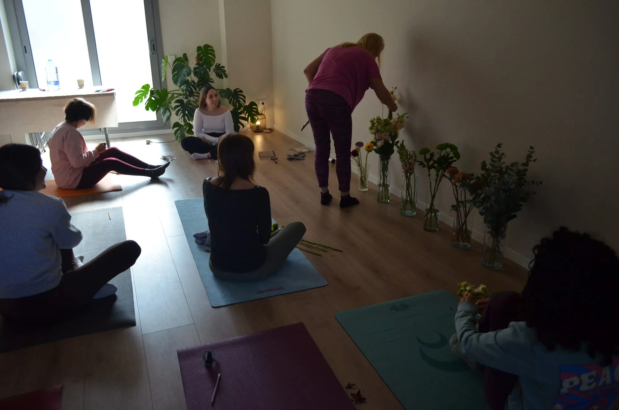 Participantes eligiendo flores de los jarrones al fondo de la sala mientras otras montan sus ramos en las esterillas