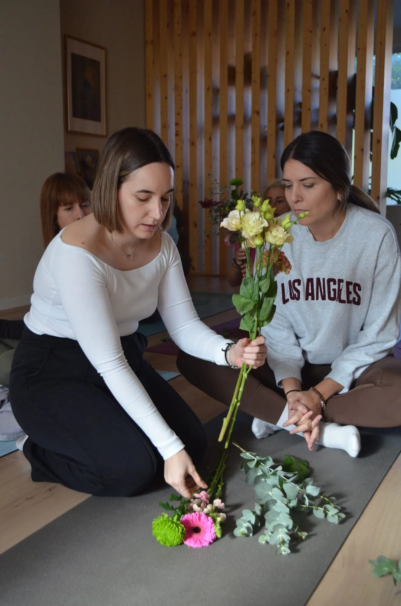 La florista ayuda a una participante a colocar los tallos de su ramo, con gerberas y crisantemos verdes en el suelo