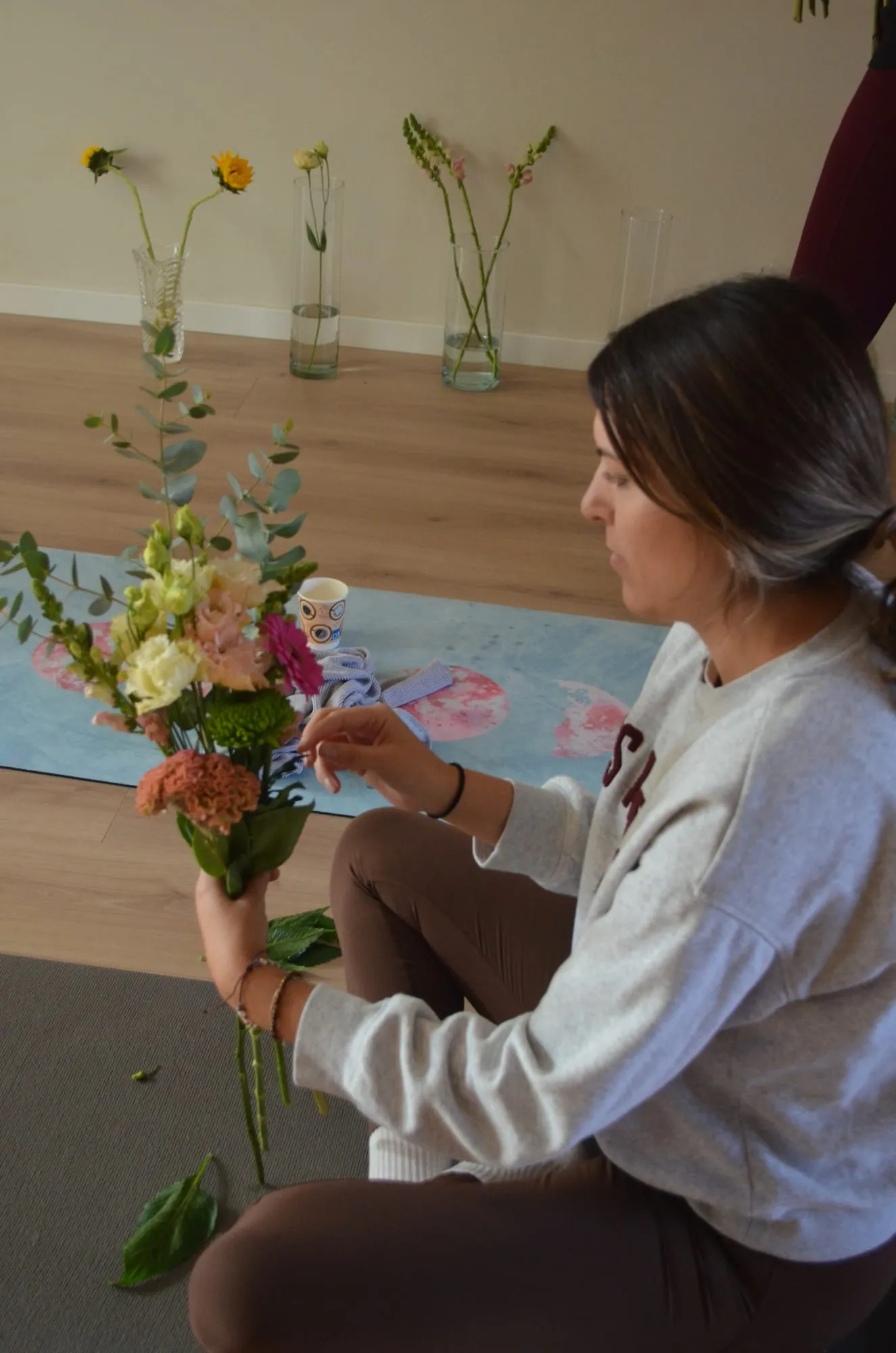 Una participante con sudadera gris añade eucalipto a su ramo de alstroemerias, gerbera y celosía