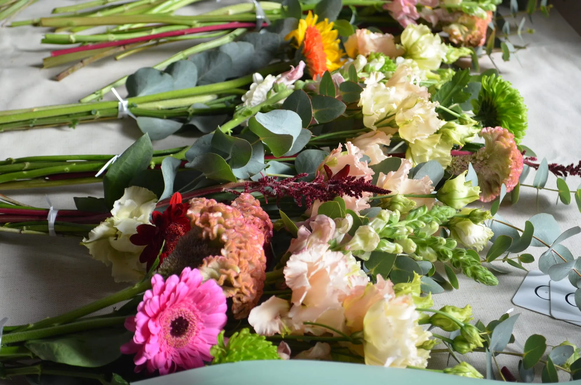 Los ramos terminados tumbados sobre una mesa: gerberas, girasol, alstroemerias, celosía, crisantemos verdes, boca de dragón y eucalipto