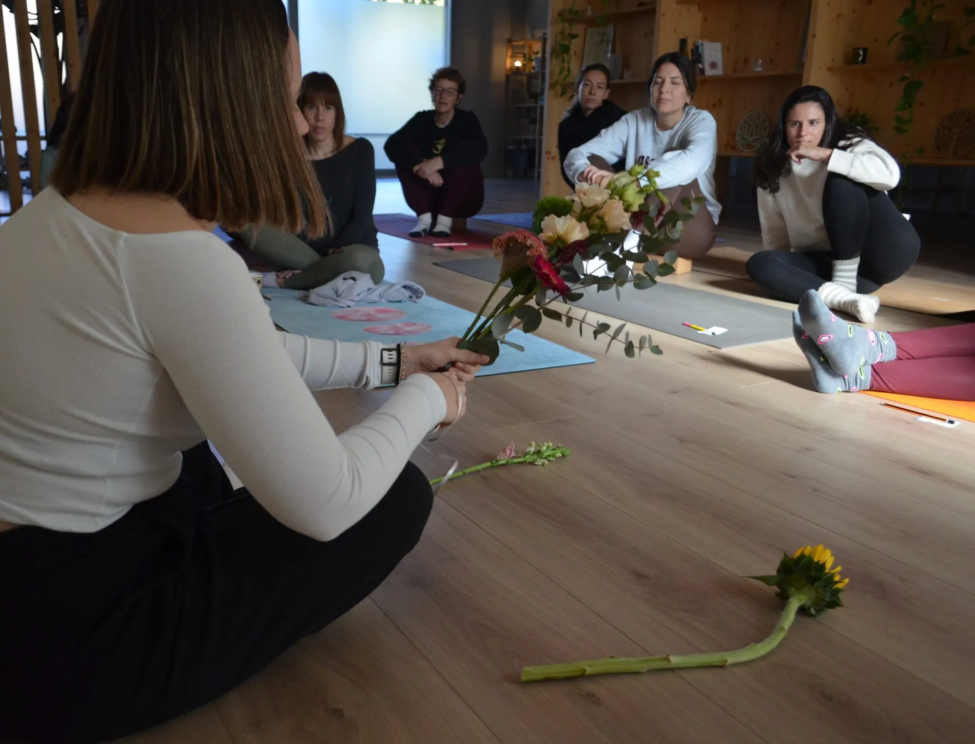 De espaldas, la florista sostiene un ramo frente al grupo, con un girasol en el suelo